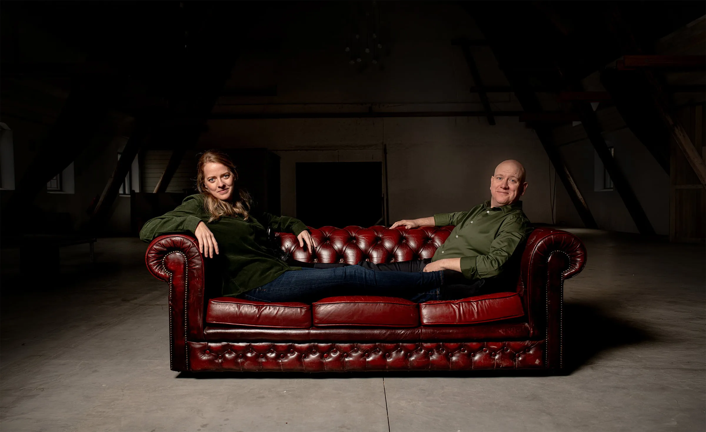 Fanny och Olof i en röd chesterfieldsoffa i en industrilokal